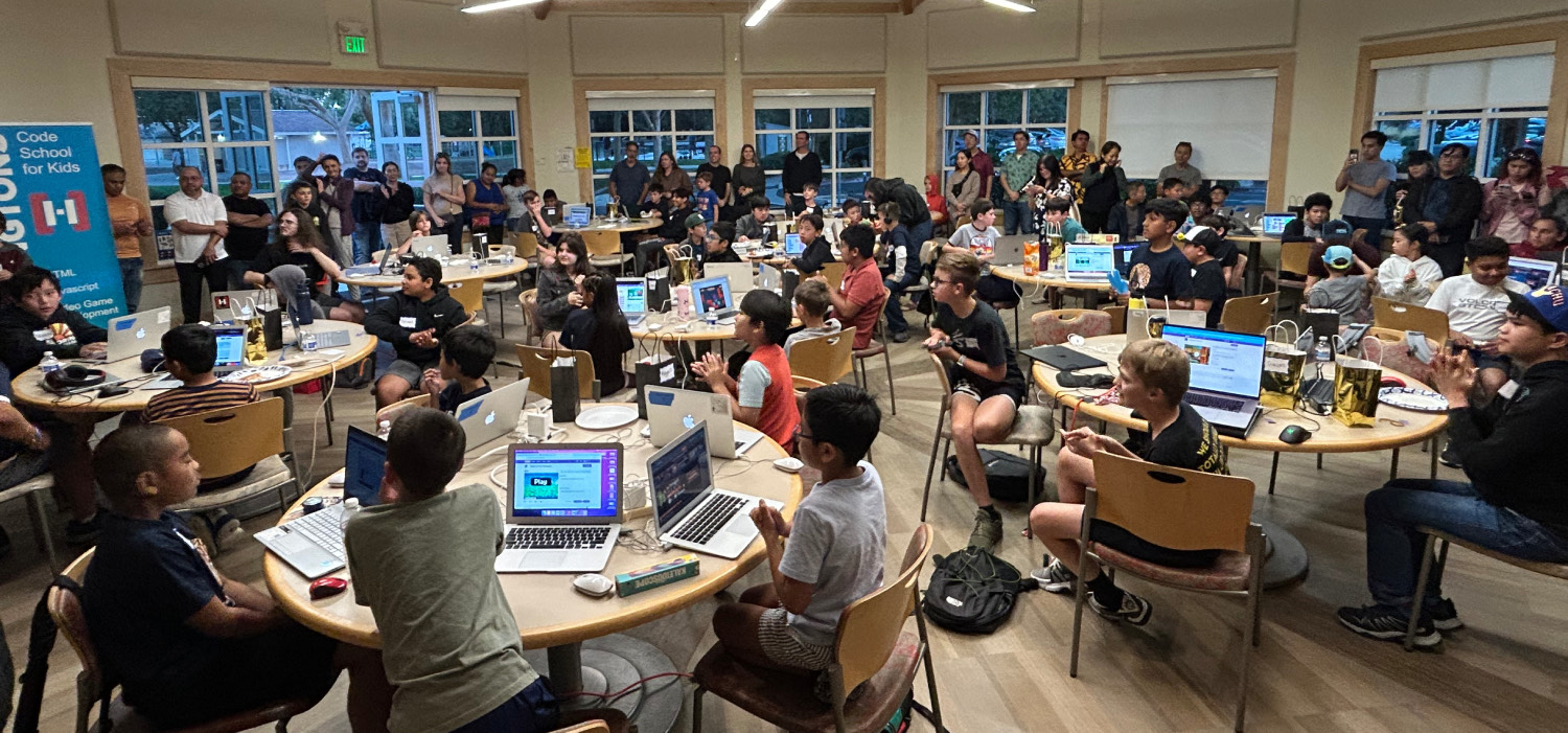 Kids competing at the 2024 Hackingtons500 coding competition while parents watch