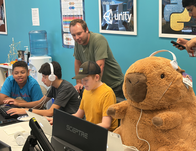 An instructor helping students at the Hackingtons Rocklin anniversary party, with the Hackingtons capybara mascot