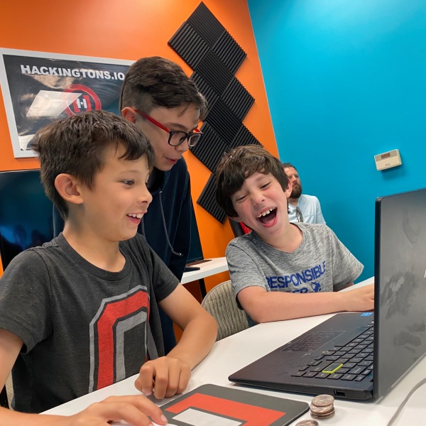 Three Hackingtons students crowded around a laptop, laughing at a game on the screen.